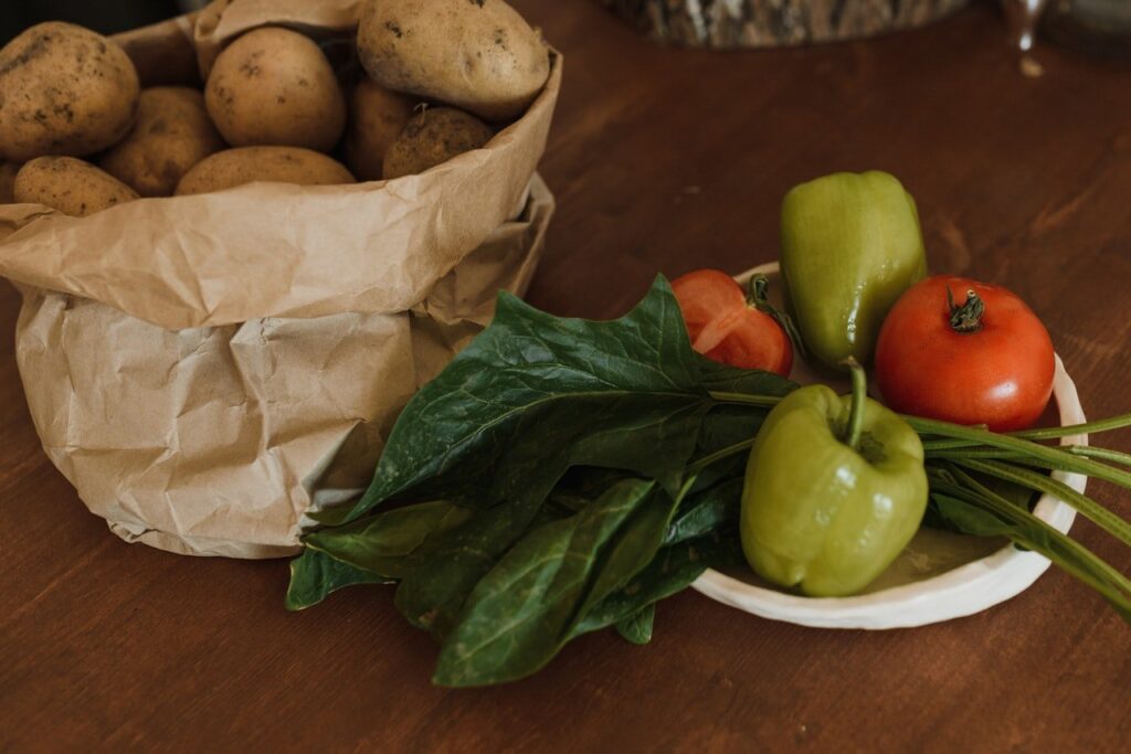 mesa com saco de batatas, folha de couve e pimentões