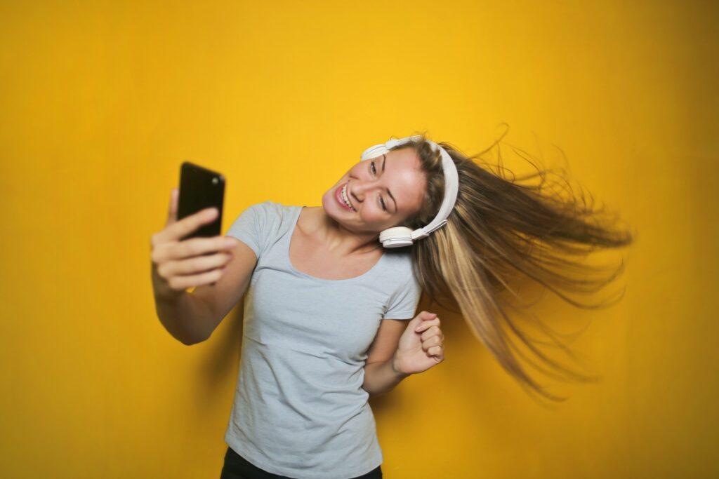 Mulher dançando, usando fones de ouvido sem fio, olhando para o celular. Demonstrando uma forma de como usar o aplicativo Treino Aeróbico para Zumba para assistir aulas online e treinar em casa