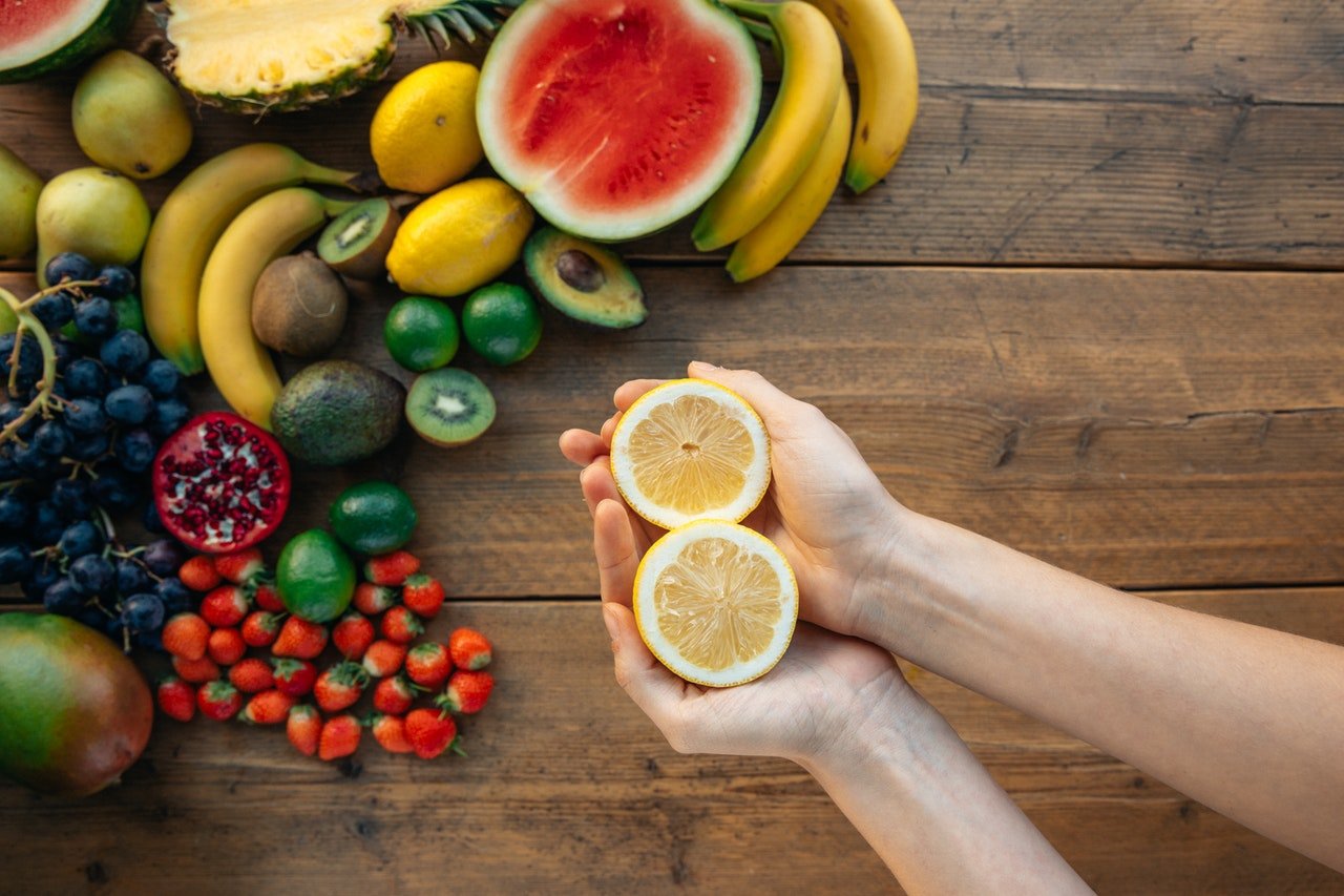 pessoa segurando uma laranja cortada ao meio junto com frutas que emagrecem ao fundo