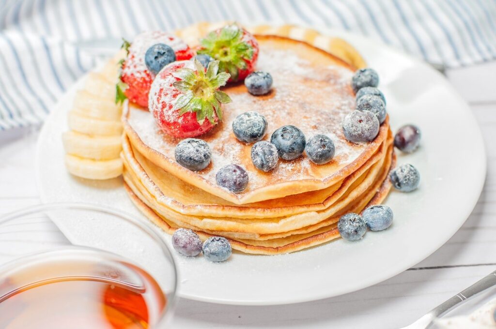 panquecas doces num prato com açúcar e algumas frutas, como morangos e uvas