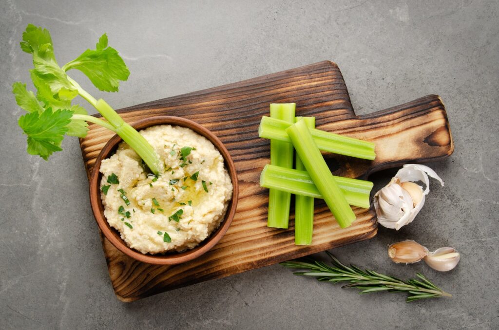 tábua de madeira com talos de salsao e tigela de pasta decorada com salsao