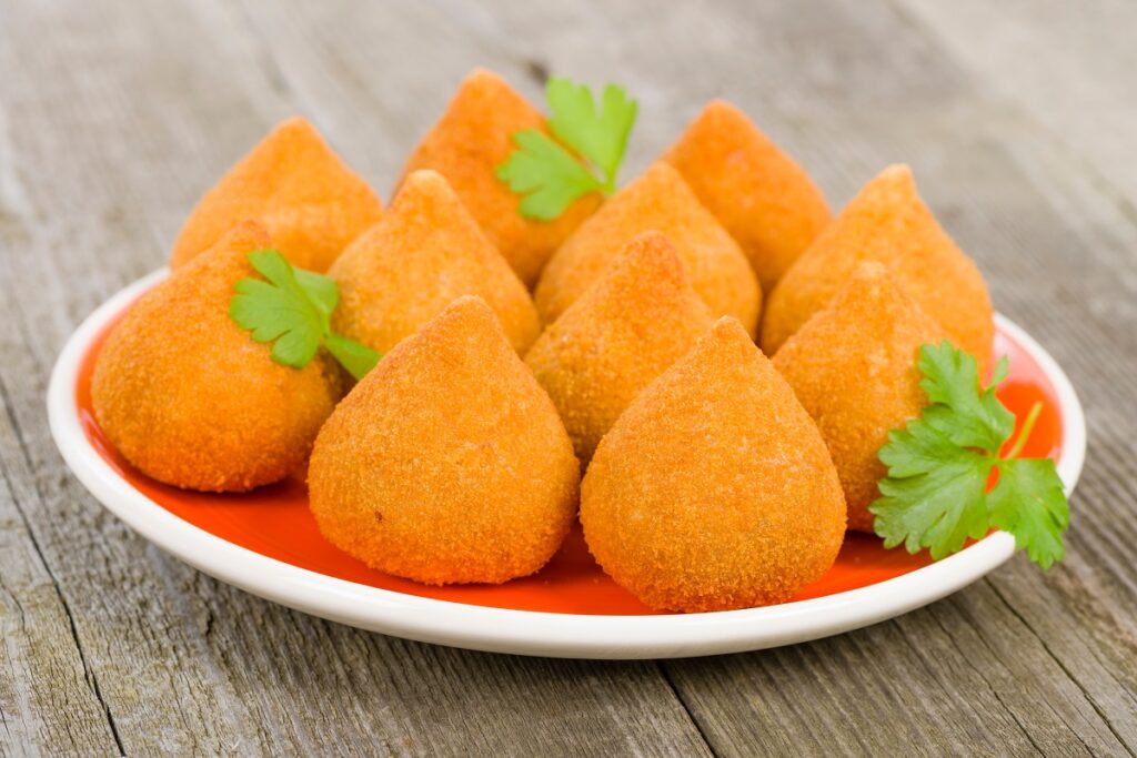 Várias coxinhas em prato vermelho junto com folhas decorativas