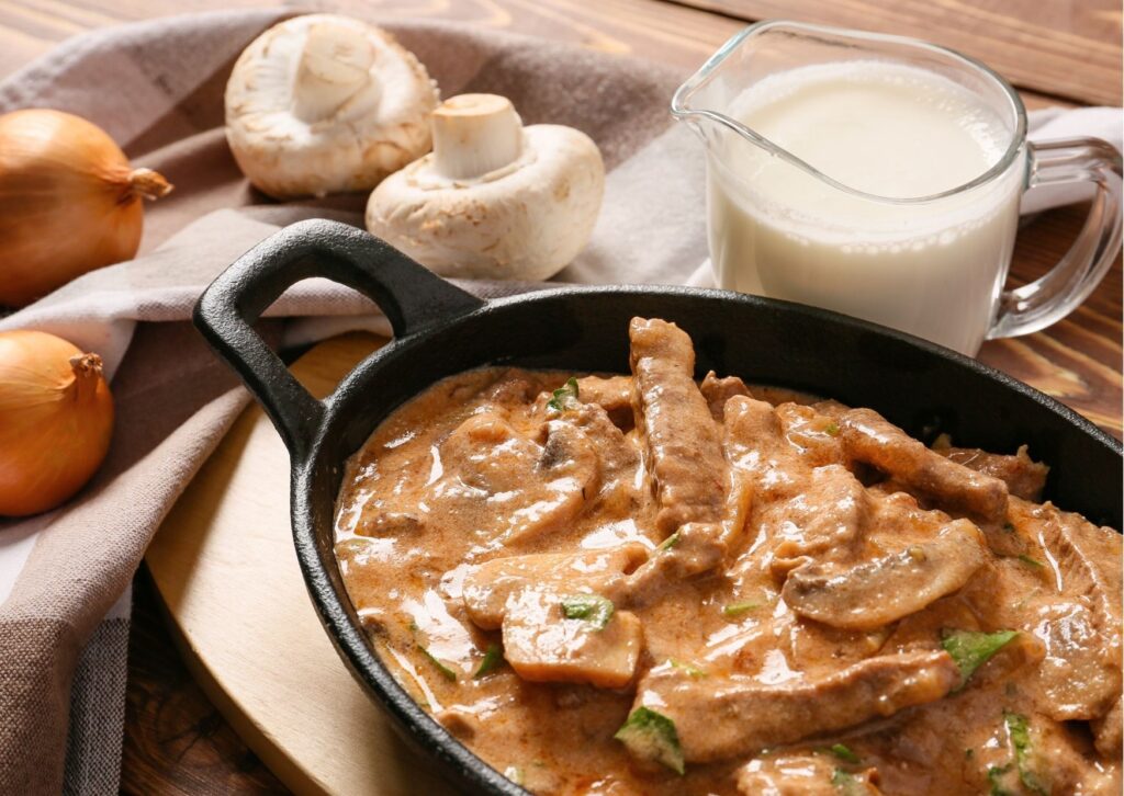 panela com strogonoff de carne de soja perto de jarra de leite, cogumelos e cebolas