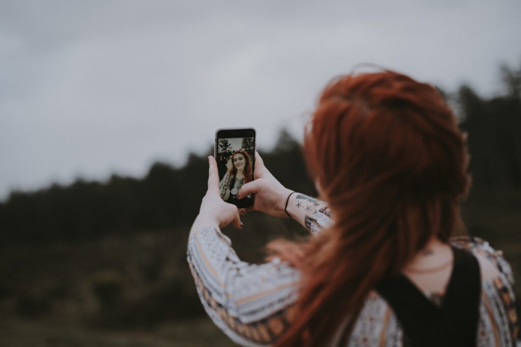 Mulher tirando selfie ao ar livre, seu rosto aparece na tela do celular, ela poderá editar a foto no Aplicativo Facetune