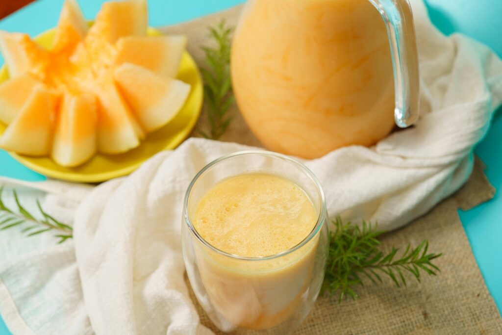 Melão cortado em fatias, jarra e copo de shake de melão. Shake de frutas com leite vegetal e whey protein está entre as opções de comida leve para noite.