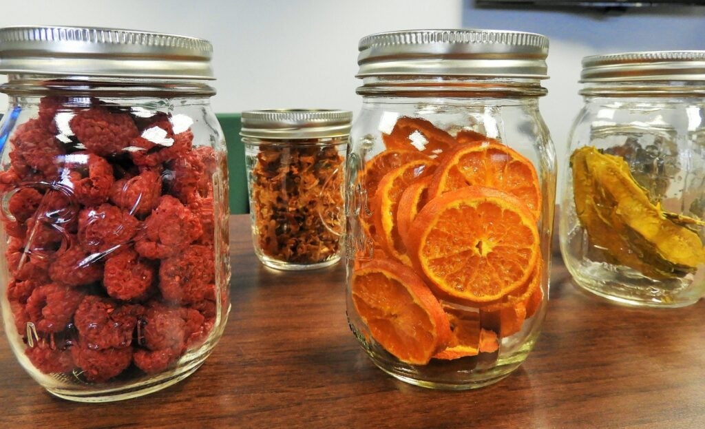 Comida liofilizada em potes de vidro, como laranja, banana e outros alimentos secos.