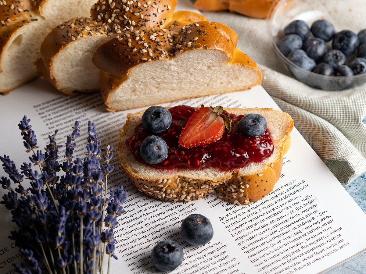 fatia de pão com geleia de frutas caseiras em cima de página de livro; ao lado, o resto do pão e outras frutas
