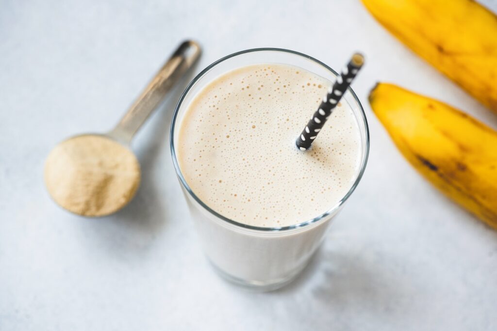 shake em copo de vidro com canudo ao lado de banana e colher de shake em pó