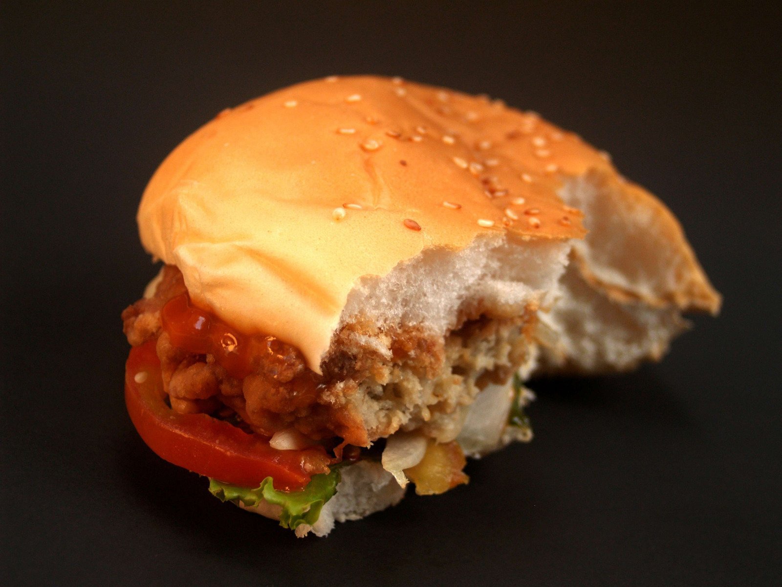 Receita de pão com hambúrguer de grão de bico, acompanha alface, tomate e ketchup. Fundo preto.