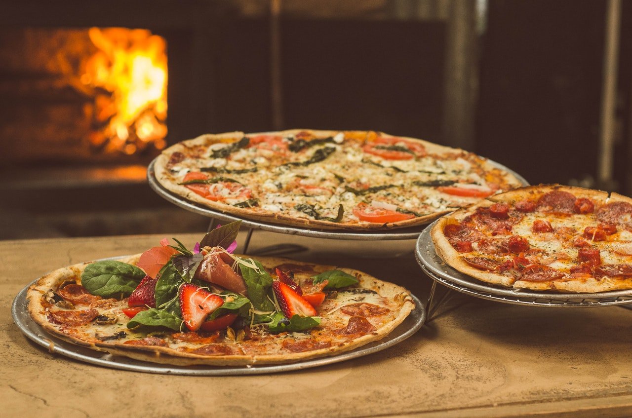 três pizzas dispostas em apoio de madeira perto de forno a lenha