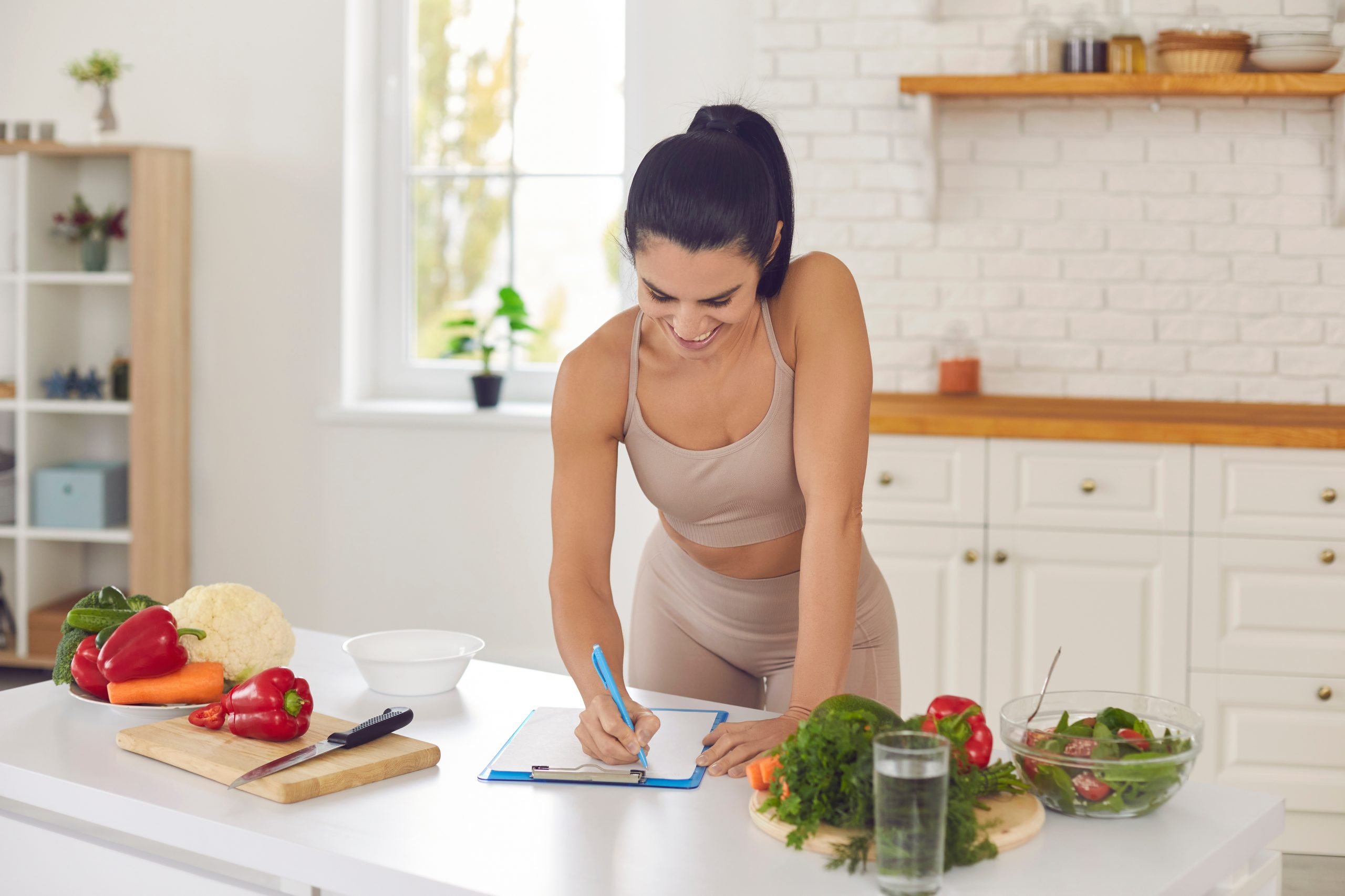 Mulher magra escrevendo receita em cozinha