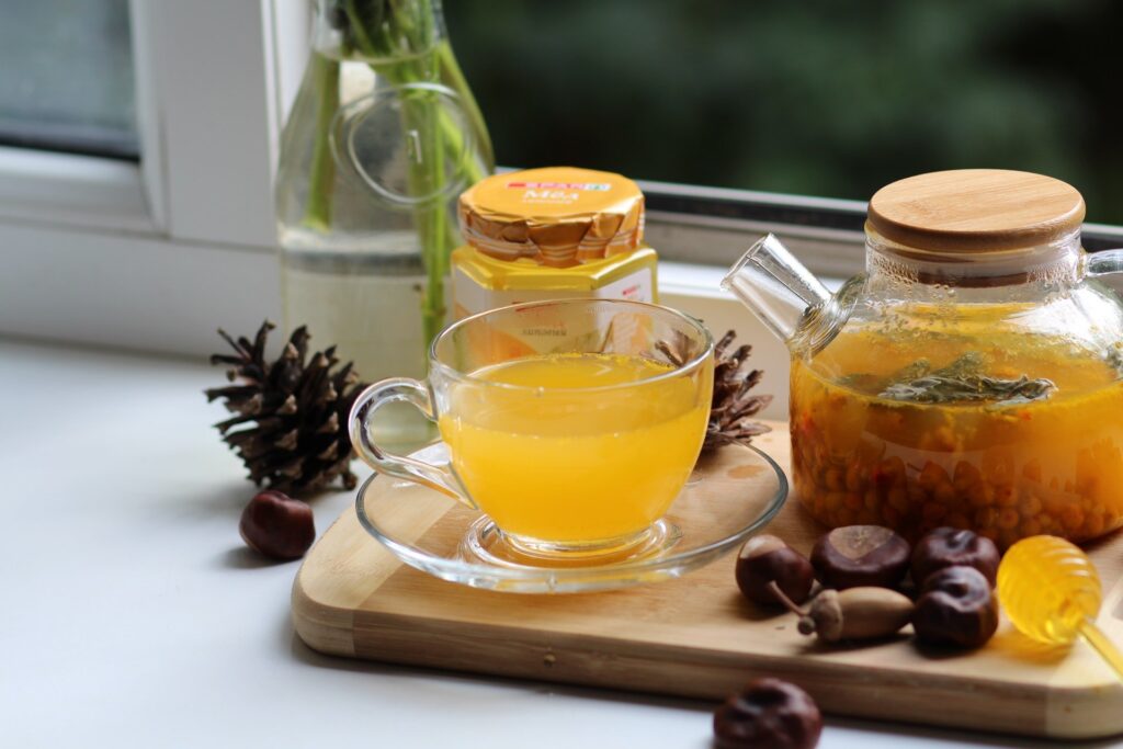 Xícara com líquido amarelo, jarro com líquido laranja, ambos sobre tábua em superfícies na cozinha. Simbolizando como tomar açafrão para emagrecer