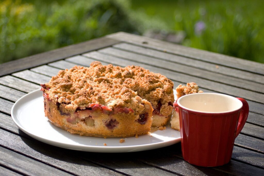 Torta de nutella com leite ninho sobre uma mesa de madeira em ambiente externo, com caneca ao lado da torta. Esse tipo de torta é uma opção entre as receitas fáceis doces