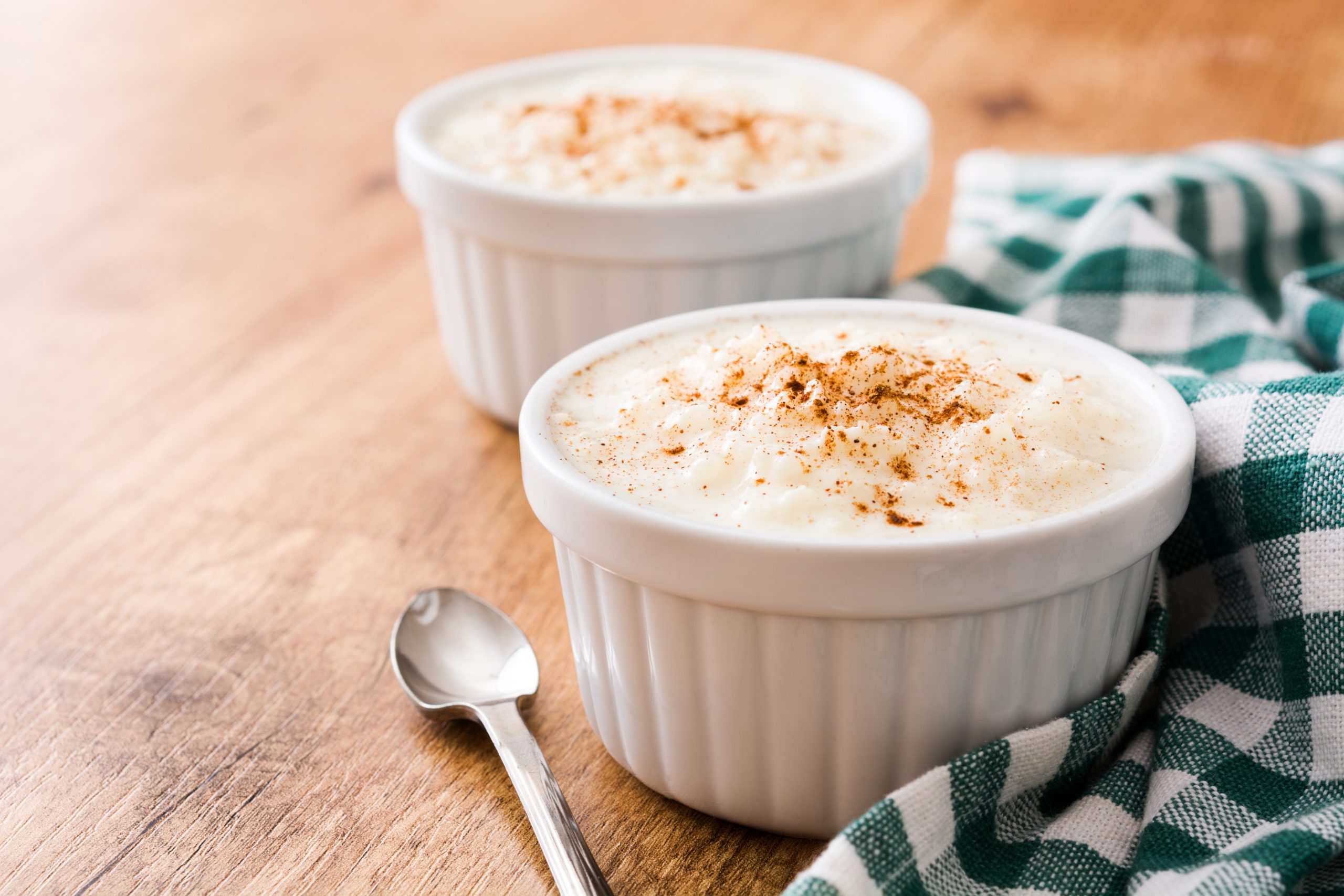 Sobre a mesa: pano de prato xadrez, colher de sobremesa e dois potes de arroz doce, com canela polvilhada por cima. Arroz doce está entre as receitas fáceis doces