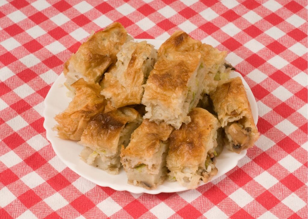 Imagem com fundo xadrez vermelho com uma torta vegetariana junina cortada em pedaços