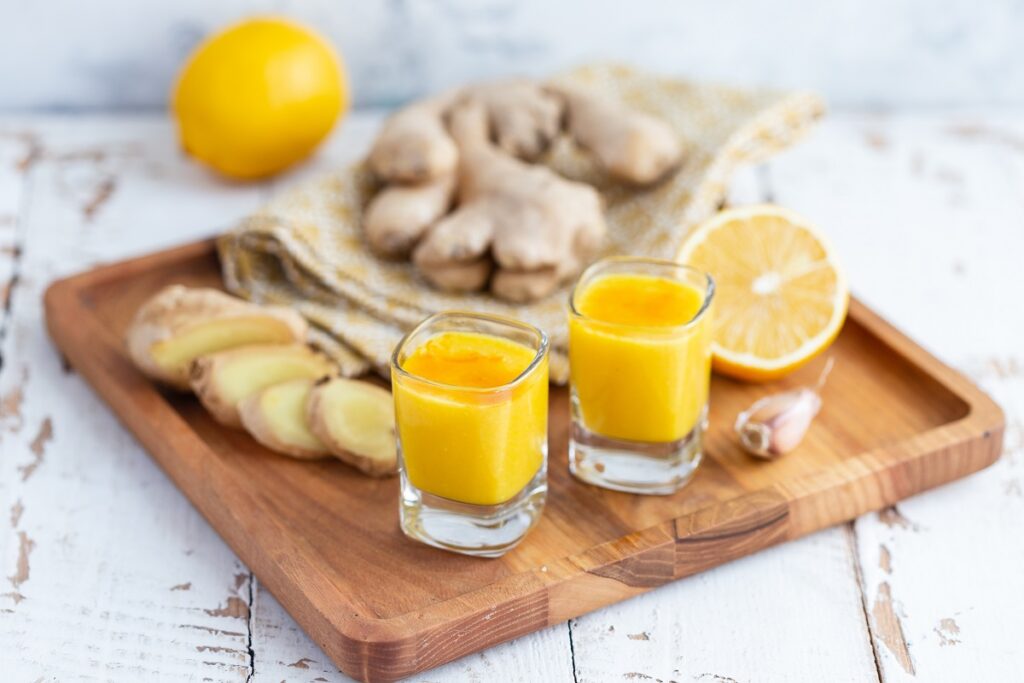 shot matinal de laranja e gengibre em dois copos de vidro colocados em cima de tábua de madeira