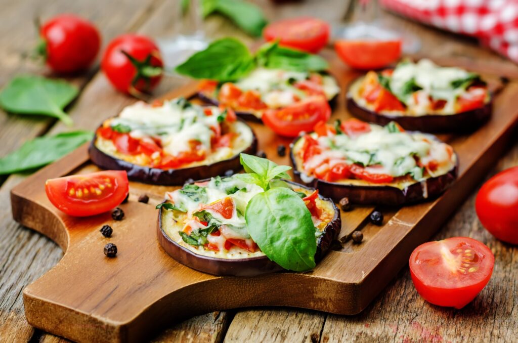 Mini pizza de berinjela, com tomates e folhas sobre tábua de madeira. A mini pizza é uma das 3 receitas com berinjela