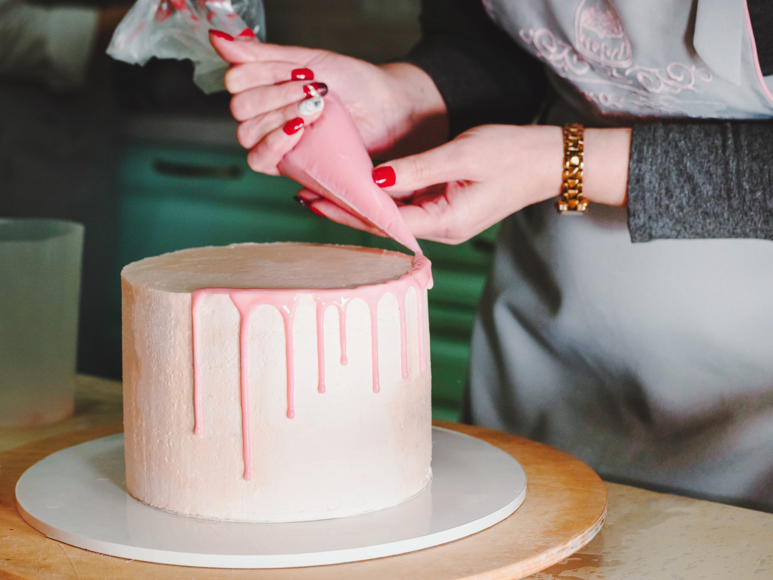 Mulher decorando bolo com bisnaga rosa rosa em prato branco