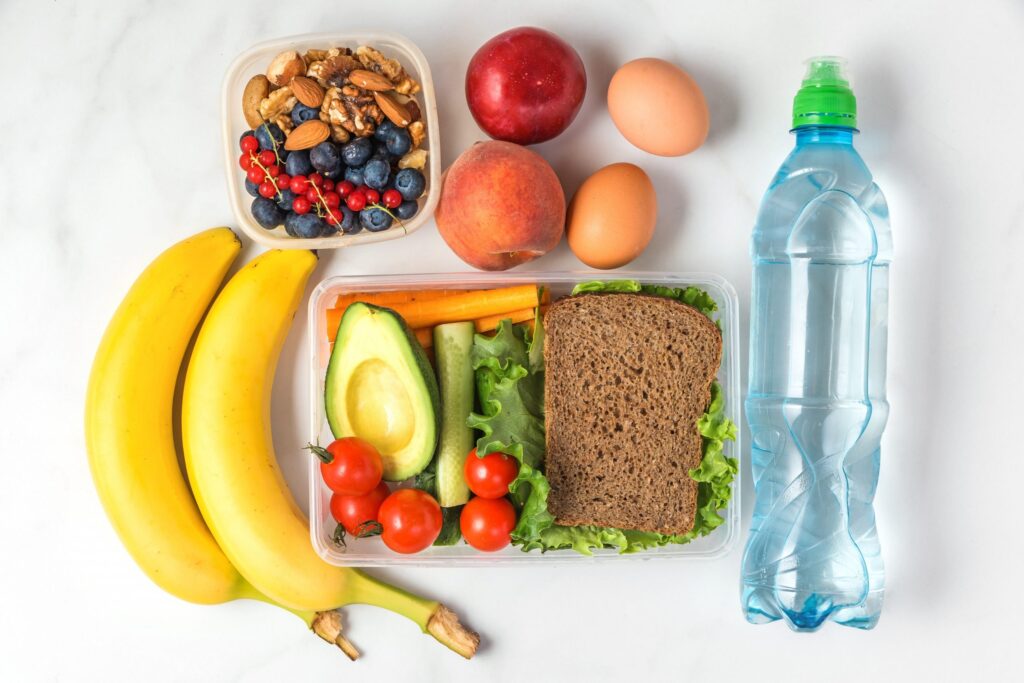 Alimentos saudáveis com sanduíche, legumes, nozes, frutas, banana, ovos, pêssegos e água no fundo de mármore branco