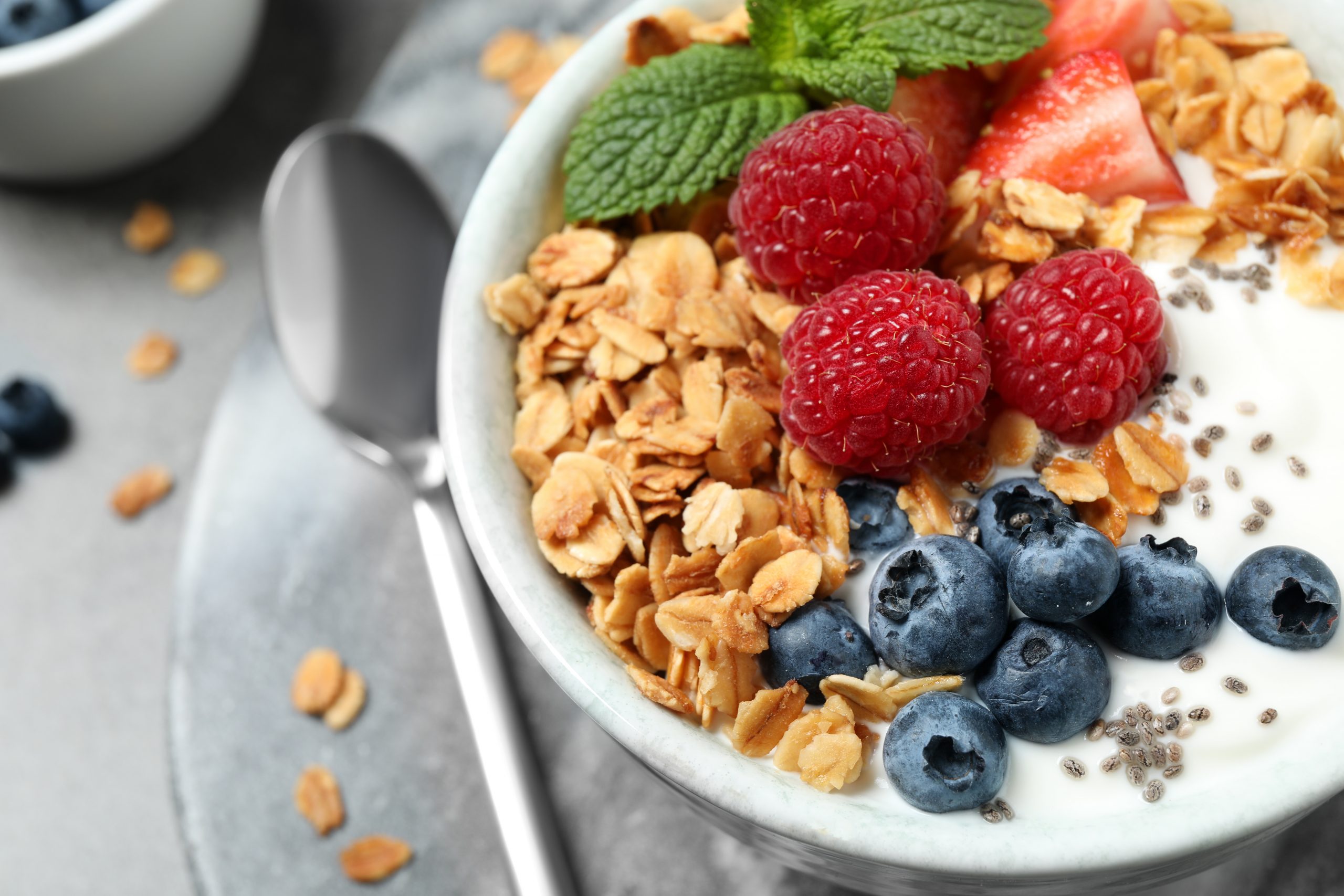 Granola caseira com iogurte e frutas em cima de mesa cinza