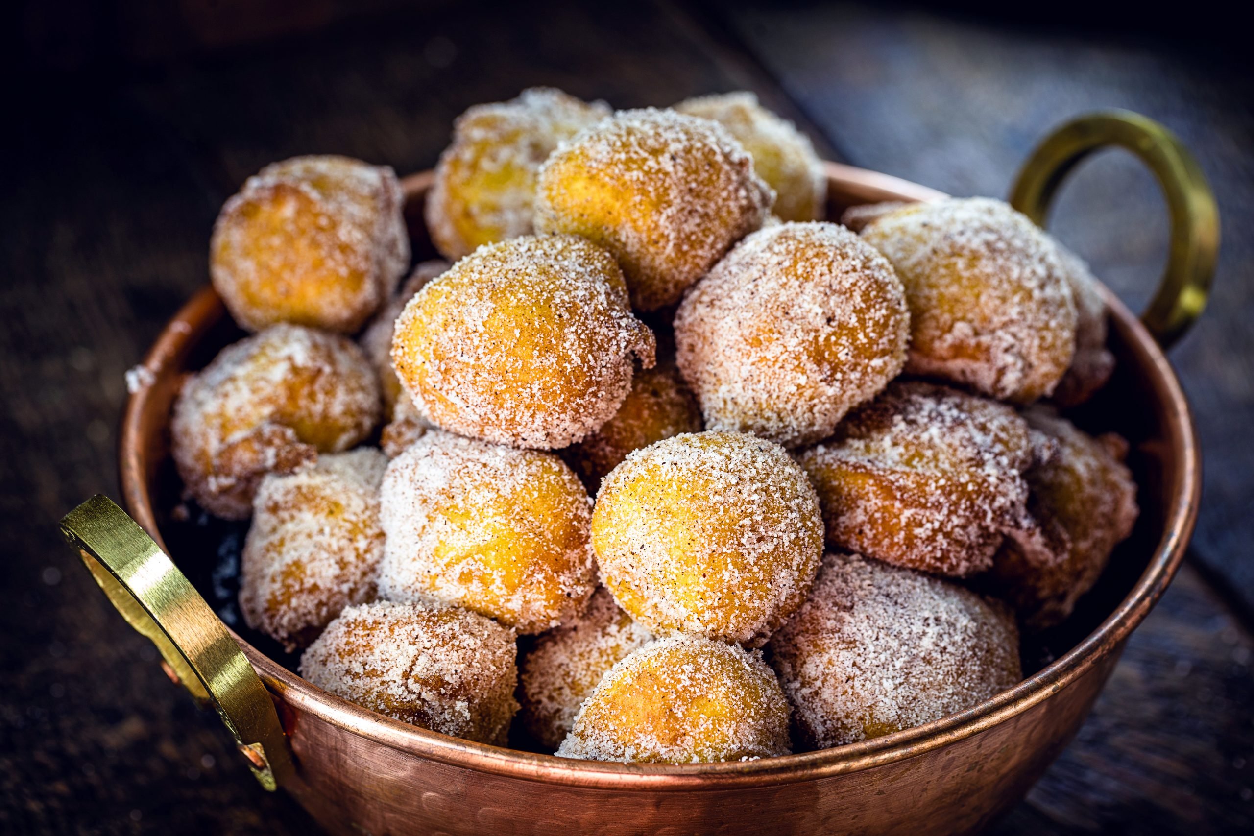 Bolinhos de chuva com açúcar e canela dentro de tacho de cobre em fundo escuro
