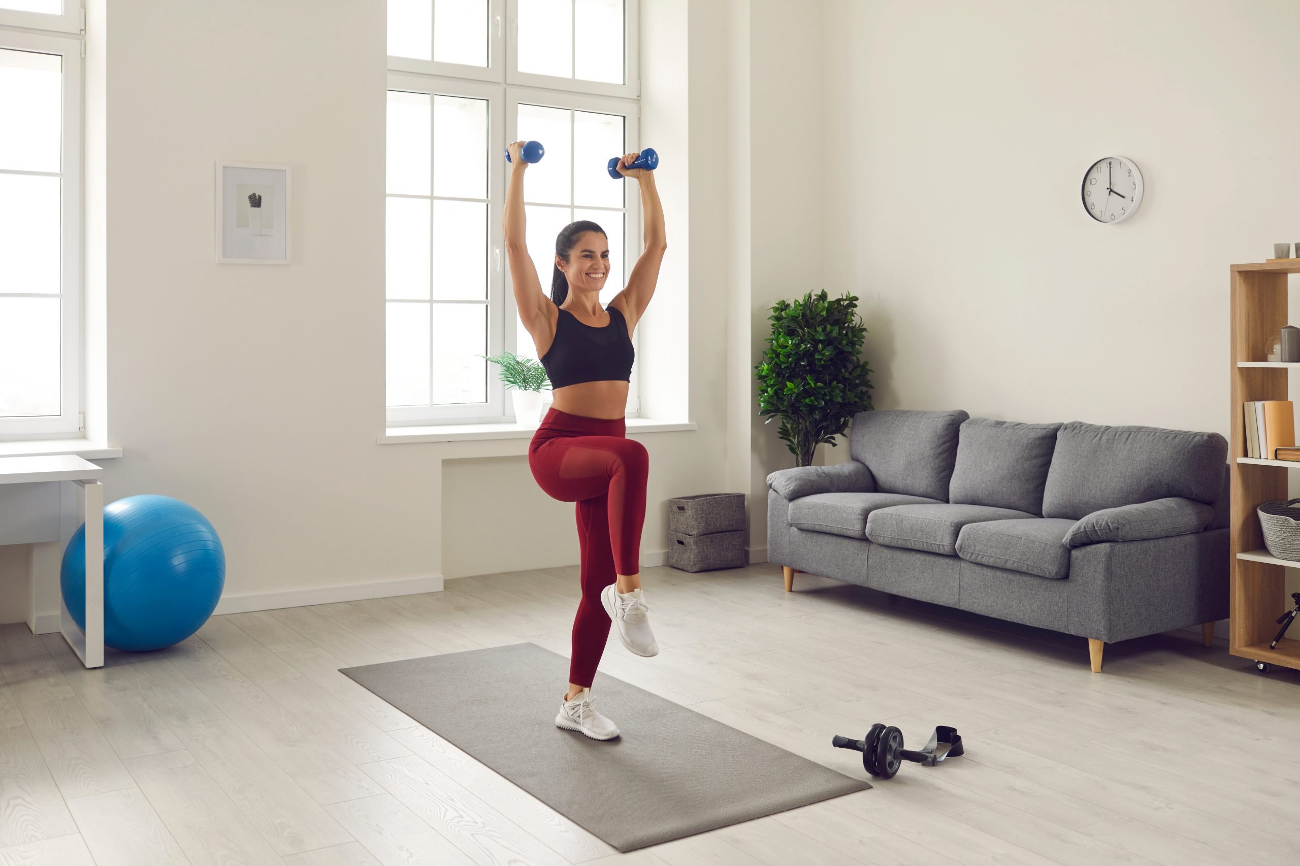 Mulher feliz em roupas esportivas fazendo exercícios com halteres durante treino em casa
