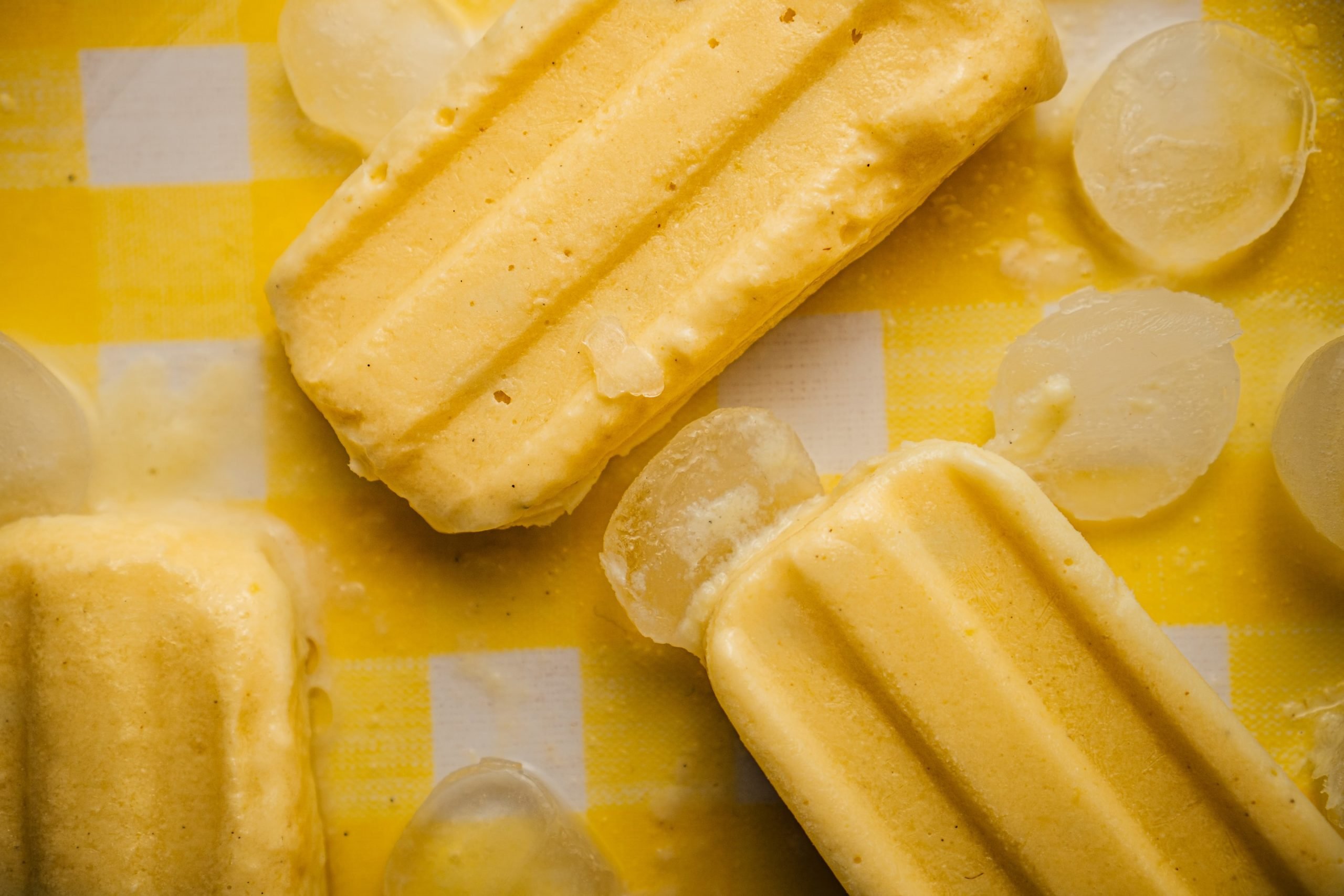 Três unidades de picolé de banana aparentemente cremoso, com gelo ao redor, derretendo