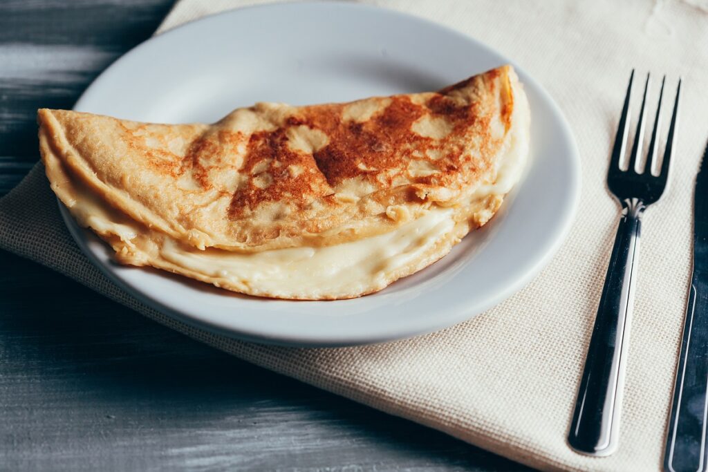 crepioca de queijo em prato branco ao lado de garfo e faca