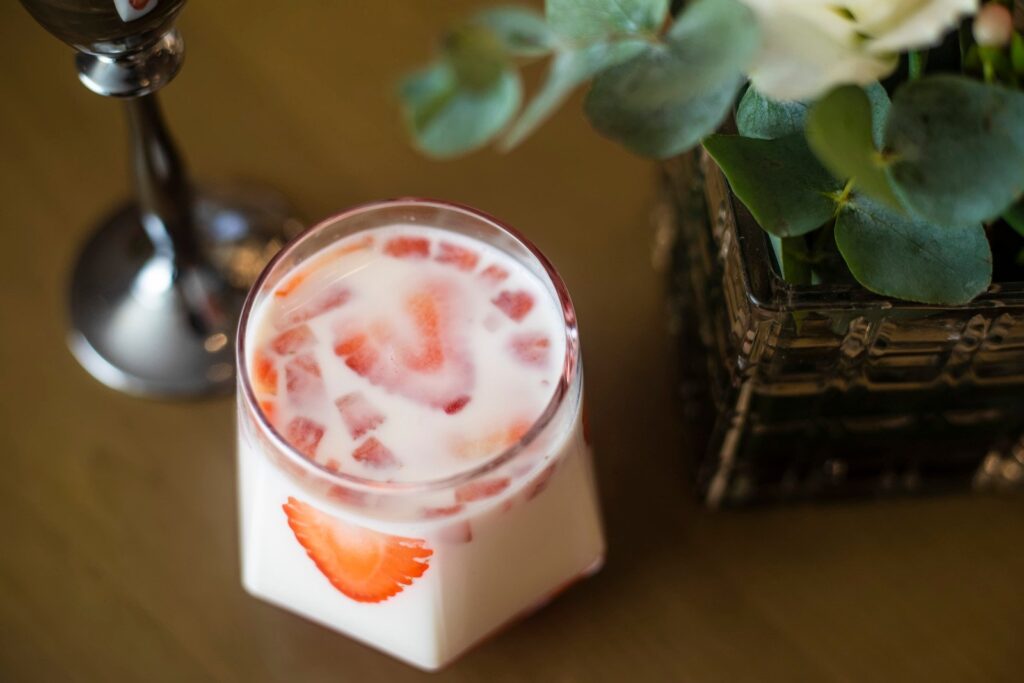 Pote de vidro com mousse de morango sobre mesa de madeira, com vaso de planta ao lado dele,