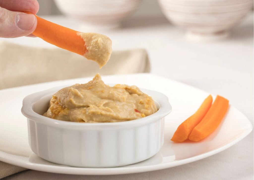 Imagem com palitos de cenoura mergulhado em hummus