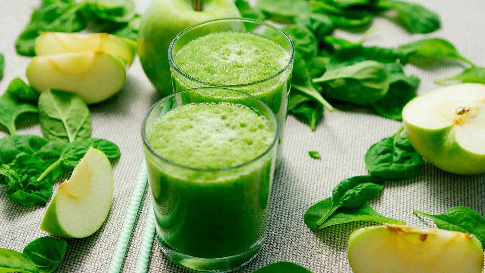 Dois copos com suco verde detox seca barriga, maçã verde e folhas ao redor dos copos