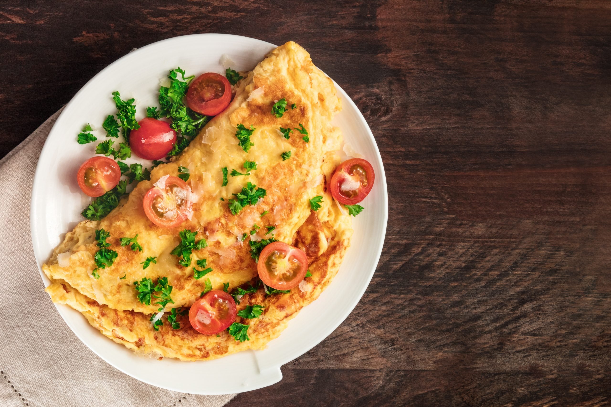 Omelete com tomate cereja e salsinha, em cima de madeira rústica