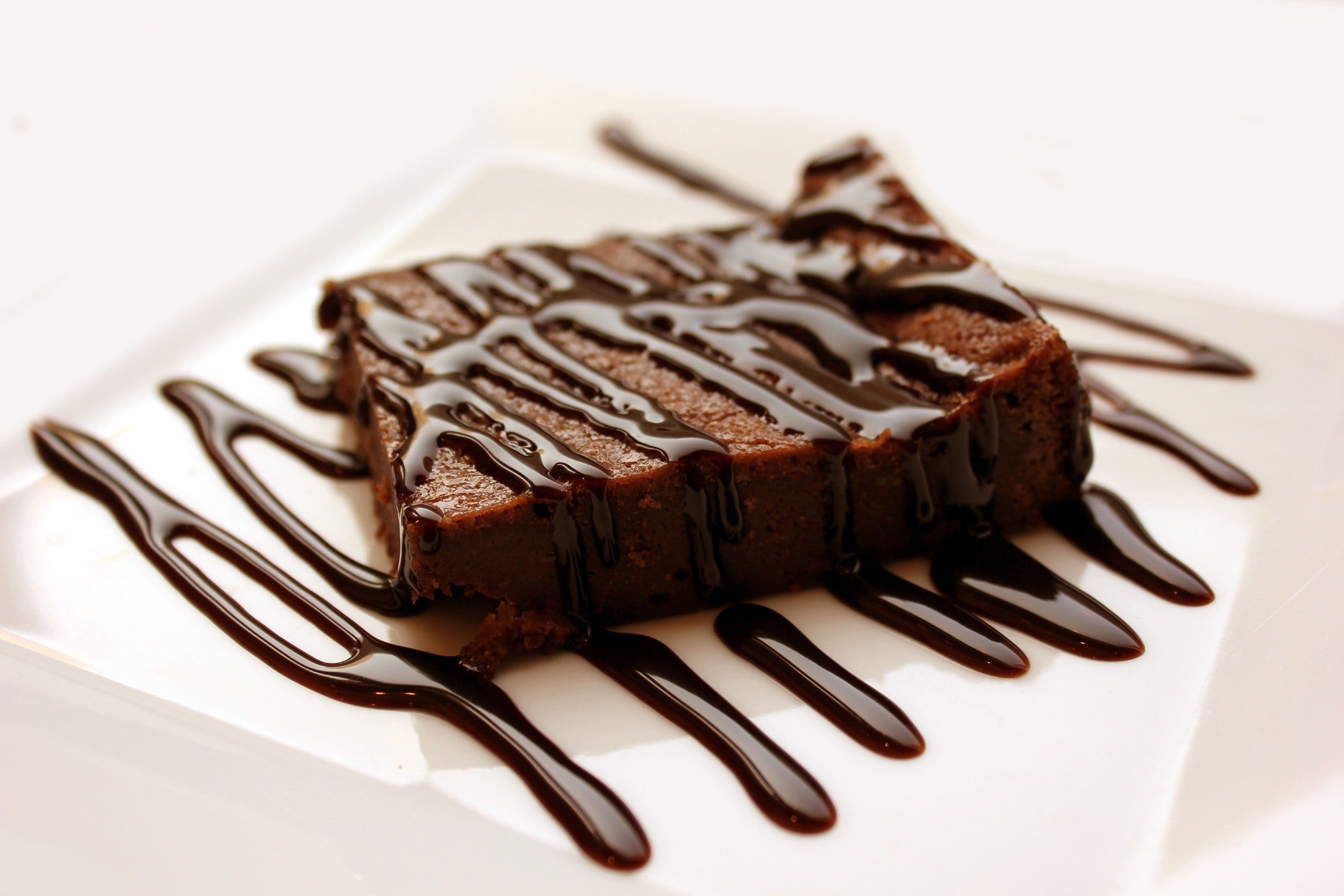 Bolo de chocolate com calda em cima de prato branco.