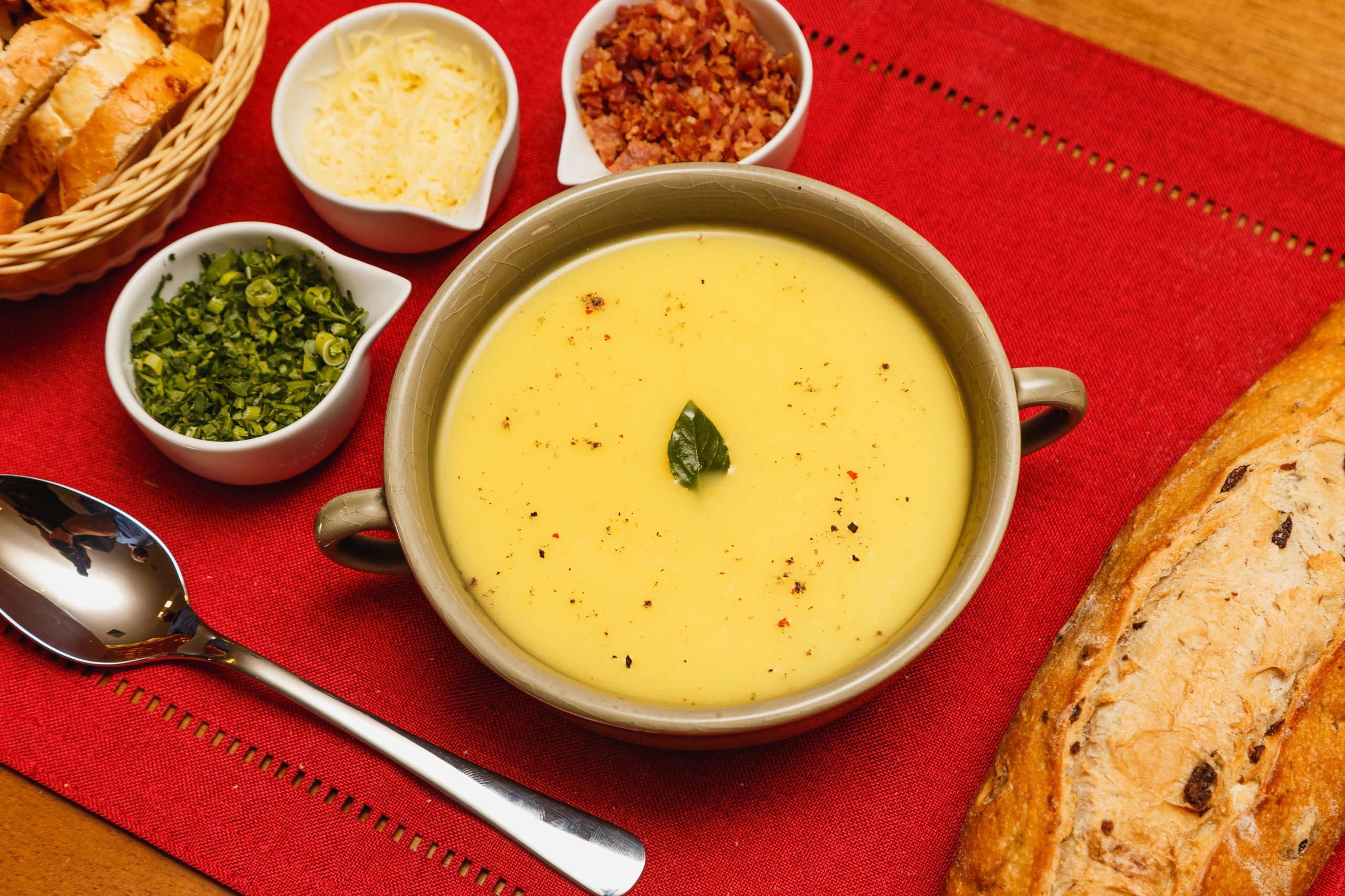 Delicioso caldo de mandioca e salsa, com fundo de madeira e tecido vermelho.