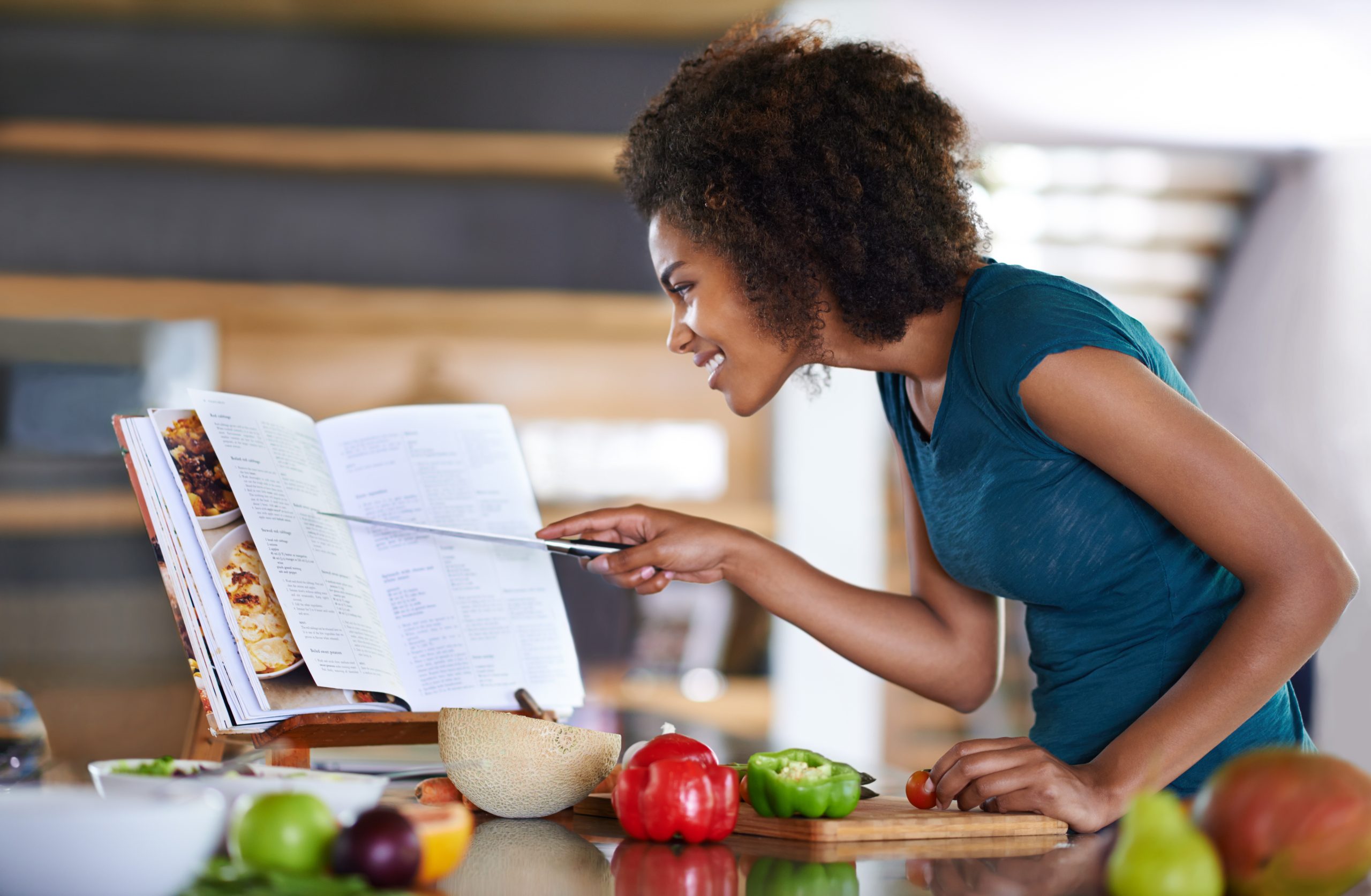 Mulher cozinhando e olhando livro de receitas
