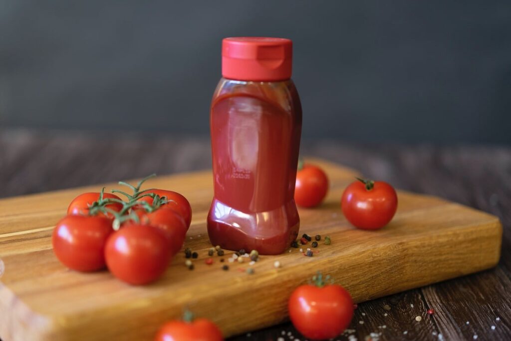 pote de katchup caseiro em cima de tábua de madeira; ao lado, alguns tomates pequenos