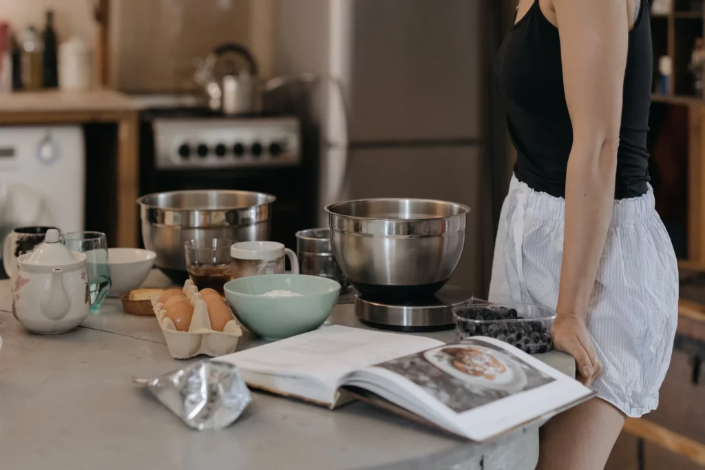 Mulher olhando ingredientes e livro de receitas