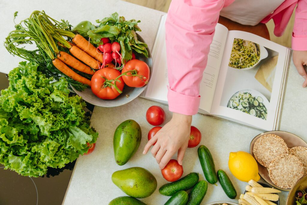 Mulher selecionando ingredientes com livro de receitas aberto